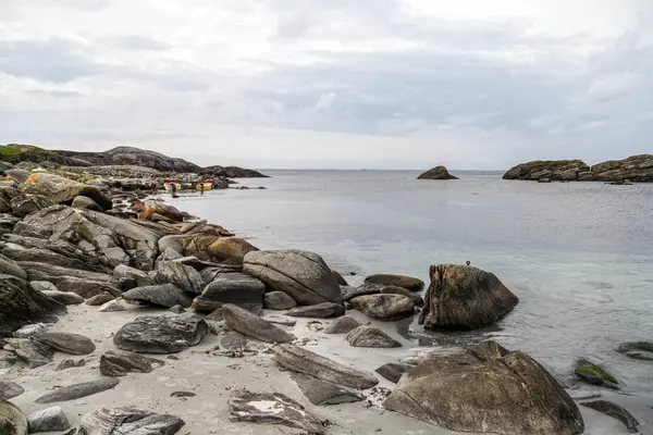 Norveç 'in arka planında büyük bir su kütlesi olan kayalık bir plaj. Kayalar sahile saçılmış ve su sakin. Sahnenin sakin ve huzurlu bir atmosferi var.