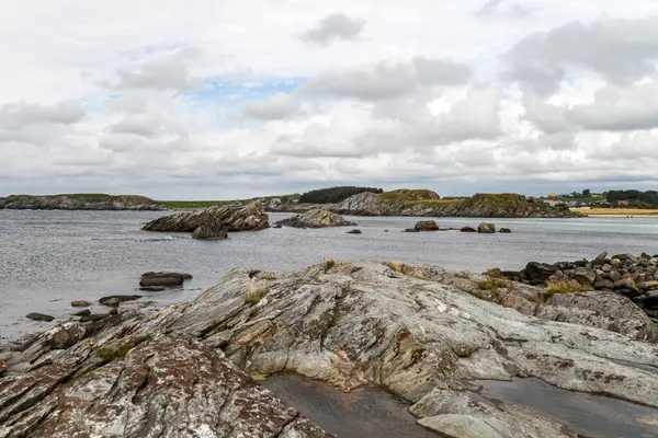 Norveç 'in arka planında bir su kütlesi olan kayalık bir kıyı şeridi. Kayalar büyük ve pürüzlü ve su sakin. Sahne huzurlu ve sakin, kayalıklarla