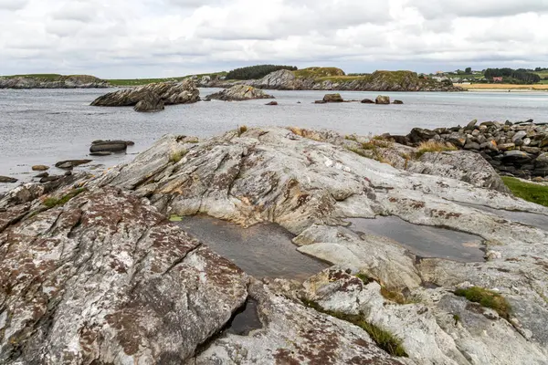 Norveç 'in arka planında bir su kütlesi olan kayalık bir kıyı şeridi. Kayalar büyük ve pürüzlü ve su sakin. Sahne huzurlu ve sakin, kayalıklarla