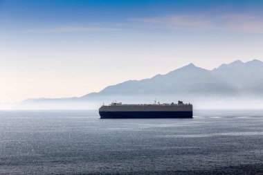Arka planda Korsika dağları olan büyük bir gemi Akdeniz 'de hareket ediyor. Gökyüzü açık ve su sakin.