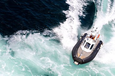 Bir tekne, Sardunya adası yakınlarında arkasında bir uyanışla denizde seyahat ediyor. Tekne siyah beyaz.