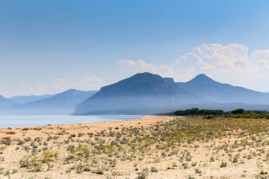 İtalya 'nın Sardunya adasında arka planda bir dağı olan güzel bir sahil. Gökyüzü açık ve güneş parlıyor.