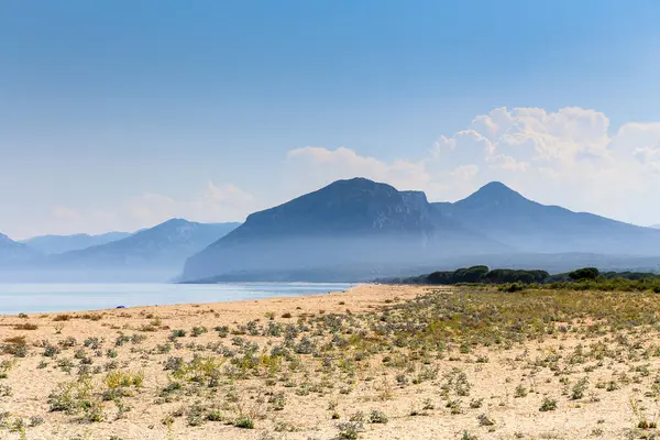 İtalya 'nın Sardunya adasında arka planda bir dağı olan güzel bir sahil. Gökyüzü açık ve güneş parlıyor.