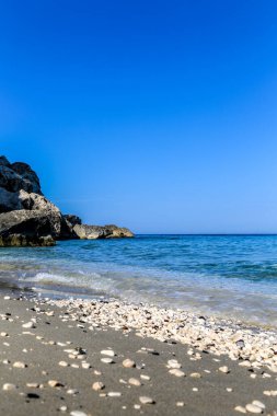İtalya 'daki Sardunya adasının arka planında berrak mavi bir okyanusu olan kayalık bir sahil. Kumsal küçük kayalar ve deniz kabuklarıyla kaplı.