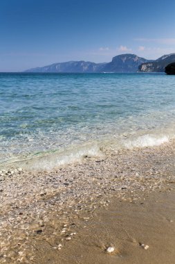 İtalya 'daki Sardunya adasının arka planında berrak mavi bir okyanusu olan kayalık bir sahil. Kumsal küçük kayalar ve deniz kabuklarıyla kaplı.