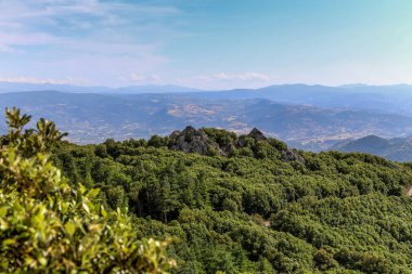İtalya 'daki Sardunya adasında açık mavi gökyüzü ile bir dağ sırası görülebilir. Dağlar ağaçlarla kaplı ve manzara huzurlu ve huzurlu.