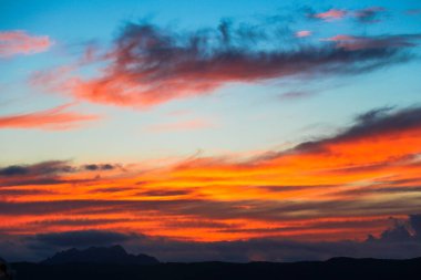 Gökyüzü bulutlarla dolu ve güneş batıyor, güzel bir turuncu ve pembe gökyüzü yaratıyor.