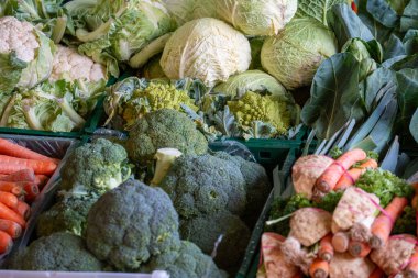Bir pazarda brokoli, havuç ve lahana gibi çeşitli sebzeler sergilenmektedir. Sebzeler taze ve renkli, canlı ve sağlıklı bir atmosfer yaratıyorlar.