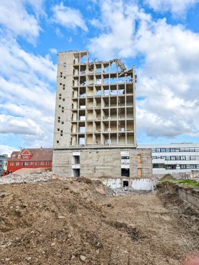 Büyük bir bina yıkım sürecinin etrafında bir sürü molozla harabe halinde. Gökyüzü bulutlu ve bina toprakla çevrili.