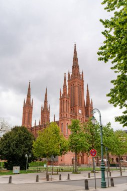 Wiesbaden Almanya 'sında Market Kilisesi' nin büyük kırmızı bir binasında saat kulesi ve kaldırımda kırmızı bir tabela vardı. Gökyüzü bulutlu ve ağaçlar yeşil