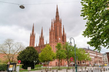 Wiesbaden Almanya 'sında Market Kilisesi' nin büyük kırmızı bir binasında saat kulesi ve kaldırımda kırmızı bir tabela vardı. Gökyüzü bulutlu ve ağaçlar yeşil