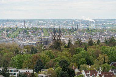 Almanya 'nın Wiesbaden şehrinin arka planında bir kilise ve orman olan bir panoraması. Şehir ağaçlar ve binalarla dolu.