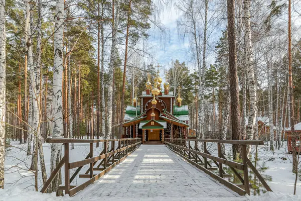 Karlı bir yolun üzerindeki tahta köprü Rusya 'nın Yekaterenburg kentindeki Ganina Yama' daki ahşap bir kiliseye çıkıyor. Kilise ağaçlarla çevrilidir ve yeşil bir çatıya sahiptir. Huzur dolu bir sahne.