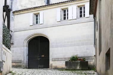 Beyaz binalı küçük bir avlu ve Konyak Fransa 'da siyah bir kapı. Kapı açık ve yerde bir saksı var.