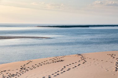Fransa 'daki kum tepeciğinde arka planda su birikintisi olan bir sahil. Su sakin ve gökyüzü mavi ve beyaz karışımı.