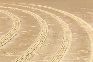 Kumsalda bir dizi lastik izi olan kumlu bir sahil. İzler kıvrımlı bir şekilde, dairesel hareket eden bir araç tarafından yapıldığını gösteriyor.