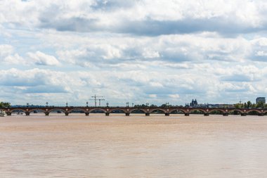 Bordeaux Fransa 'daki bir taş köprü arkasında bulutlu bir gökyüzü olan bir nehri kapsar. Köprü kırmızı tuğlalardan yapılmıştır ve suyla çevrilidir.