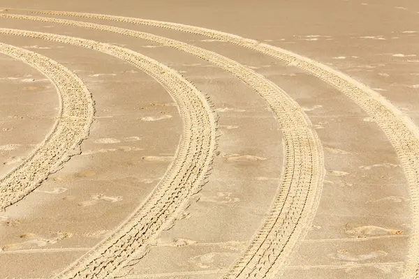 Kumsalda bir dizi lastik izi olan kumlu bir sahil. İzler kıvrımlı bir şekilde, dairesel hareket eden bir araç tarafından yapıldığını gösteriyor.
