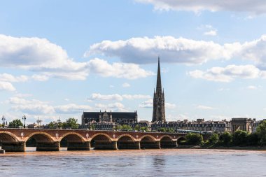 Bordeaux Fransa 'da bir taş köprü arkasında bir şehir olan Garonne nehri. Gökyüzü bulutlu ve güneş parlıyor