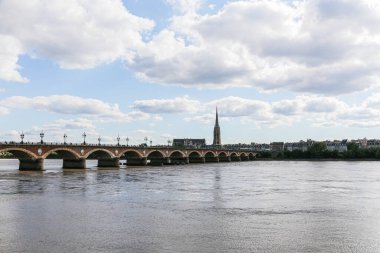 Bordeaux Fransa 'da bir taş köprü arkasında bir şehir olan Garonne nehri. Gökyüzü bulutlu ve güneş parlıyor