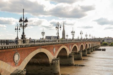 Bordeaux Fransa 'daki bir taş köprü arkasında bulutlu bir gökyüzü olan bir nehri kapsar. Köprü kırmızı tuğlalardan yapılmıştır ve suyla çevrilidir.