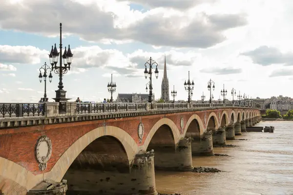 Bordeaux Fransa 'daki bir taş köprü arkasında bulutlu bir gökyüzü olan bir nehri kapsar. Köprü kırmızı tuğlalardan yapılmıştır ve suyla çevrilidir.