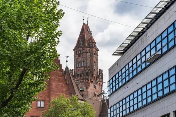 Saarbrucken Almanya 'sında önünde saat kulesi ve bir ağaç olan yüksek bir bina. Gökyüzü bulutlu ve bina beyaz.