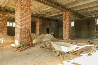 Büyük bir binanın inşaatı devam ediyor, tuğlalar ve aletli yapı malzemeleri görülebilir durumda. Duvarlar çeşitli tuğlalardan ve betondan yapılmıştır..