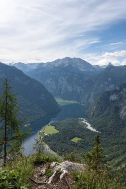 Almanya, Bavyera 'daki Koenigsee' nin yukarısından görüntü. Hava sisli güneşli, gökyüzü mavi. Göl dağlık ve etrafında yeşil dağlar var..