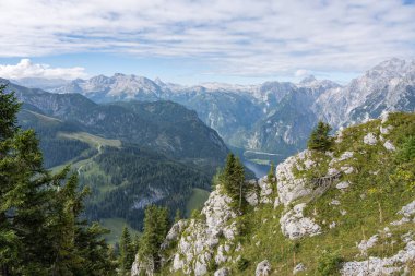 Almanya 'da, kısmen ormanla kaplı gri dağları olan güzel bir dağ manzarası. Gökyüzü mavi ve bulutlu. Dağların arasından geçen ince, dolambaçlı bir yol..