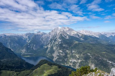 Almanya, Bavyera 'daki Koenigsee' nin yukarısından görüntü. Hava sisli güneşli, gökyüzü mavi. Göl dağlık ve etrafında yeşil dağlar var..
