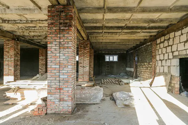 Büyük bir binanın inşaatı devam ediyor, tuğlalar ve aletli yapı malzemeleri görülebilir durumda. Duvarlar çeşitli tuğlalardan ve betondan yapılmıştır..