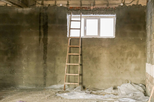 A wooden ladder leans against a freshly plastered wall. The grey wall has a built-in 3-section window.