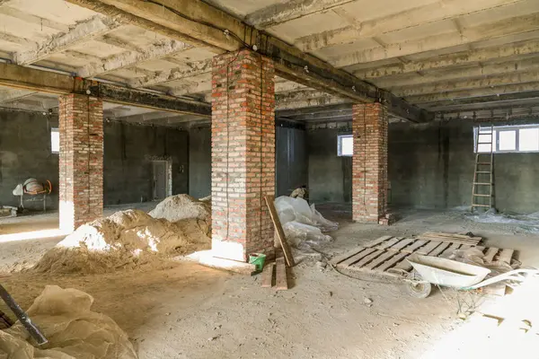 Büyük bir binanın inşaatı devam ediyor, tuğlalar ve aletli yapı malzemeleri görülebilir durumda. Duvarlar çeşitli tuğlalardan ve betondan yapılmıştır..