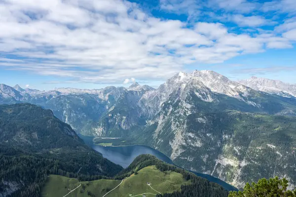 Almanya, Bavyera 'daki Koenigsee' nin yukarısından görüntü. Hava sisli güneşli, gökyüzü mavi. Göl dağlık ve etrafında yeşil dağlar var..