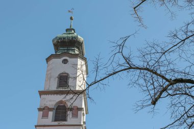Lindau, Almanya 'da tepesinde bir kubbe olan beyaz kilise kulesi. Üzerinde demir bir bayrak asılı. Fotoğrafta sağda yaprakları olmayan bir ağaç görebilirsiniz..