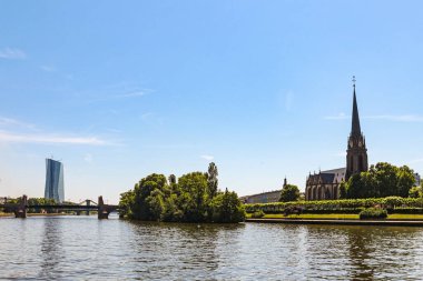 Almanya 'nın Frankfurt şehrinin güzel bir manzarası. Arkasında büyük bir kilise ve bir köprü var. Su sakin ve gökyüzü berrak.