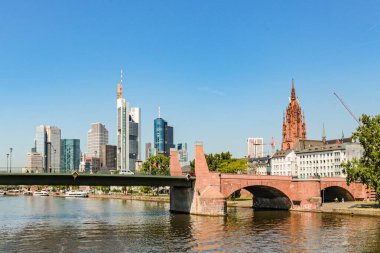 Almanya 'da bir Frankfurt şehri, mavi gökyüzünün arka planına karşı bir nehir üzerinde köprüsü olan bir ufuk çizgisi. Köprü kırmızı ve su sakin.
