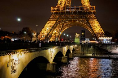 Eyfel Kulesi geceleri ışıldıyor ve güzel ve romantik bir ortam yaratıyor. Kule, bazıları ikonik simgenin fotoğraflarını çeken bir grup insanla çevrili.