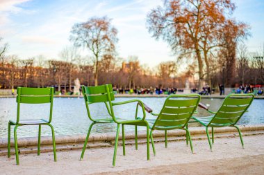 Tuileries Garden 'daki çeşmenin yanındaki parkta birkaç yeşil sandalye duruyor. Fransa 'da Paris. Fotoğraf akşamleyin çekildi. Arka planda birkaç bulut olan mavi bir gökyüzü..