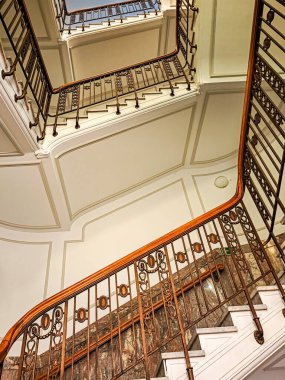 Eski bir binadaki spiral bir merdiven yukarı çıkar, ortadan vurulur. Sarmal merdiven, geçidin etrafında daire çiziyor. Duvarlar beyaz. Korkuluklar süslenmiş..