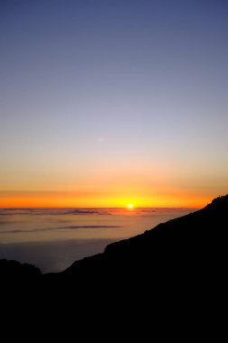 Pico de Arieiro, Madeira - Engebeli bir dağ manzarasının üzerinde güneş ufuktan yükselirken gün doğumu. Gökyüzü yumuşak maviden altın ve turuncu tonlara dönüşür.