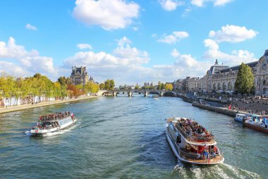 A scenic view of the Seine River in Paris, with a boat tour passing by, offering a glimpse of iconic landmarks like the Louvre and Muse d'Orsay. clipart