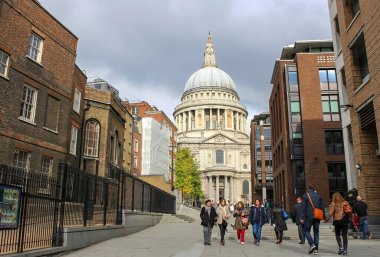 St. Pauls Katedrali 'nin önünde, modern binalarla çevrili basamaklarda yürüyen ve parçalı bulutlu gökyüzü altında....