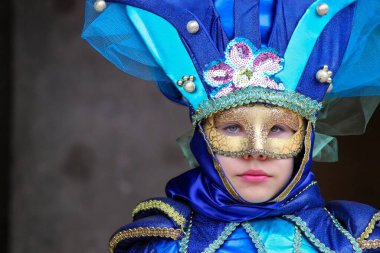 Venedik karnaval kostümü giymiş, parlak mavi tüylü başlıklı ve altın maskeli genç bir çocuğun yakın çekimi..