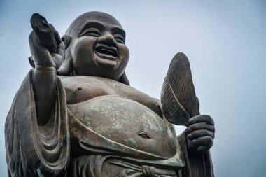 A close-up of the Laughing Buddha statue at Bai Dinh Temple, holding a fan and radiating joy. The statue symbolizes happiness, prosperity, and peace. clipart