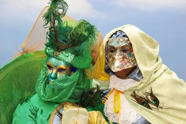Gösterişli Venedik karnaval kostümleri içinde tavus kuşu tüyleri ve altın renkli maske takan canlı yeşil bir kıyafet giyen bir çift..