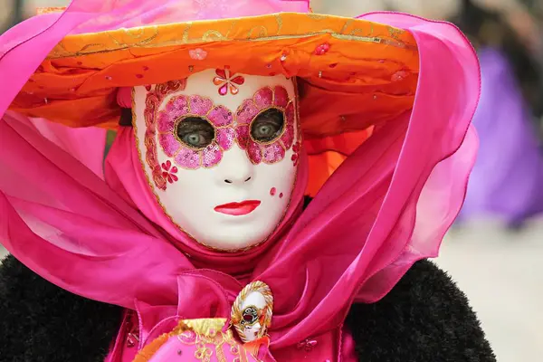 Özenle hazırlanmış pembe Venedik karnaval maskesi takmış pullarla ve çiçek desenleriyle süslenmiş bir kişi..