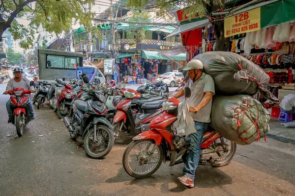 Bir adam, Hanoi, Vietnam 'ın hareketli sokaklarında motosikletinin üzerinde büyük miktarda malı dikkatle dengeler..