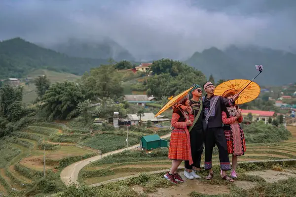 Geleneksel Vietnam kıyafetleri giymiş bir grup arkadaş, tepede sarı şemsiyeli bir selfie için poz veriyorlar..